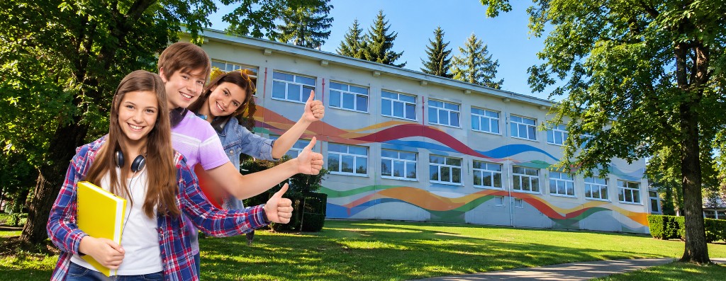 Usměvaví žáci před školní budovou s barevnou malbou na zdi